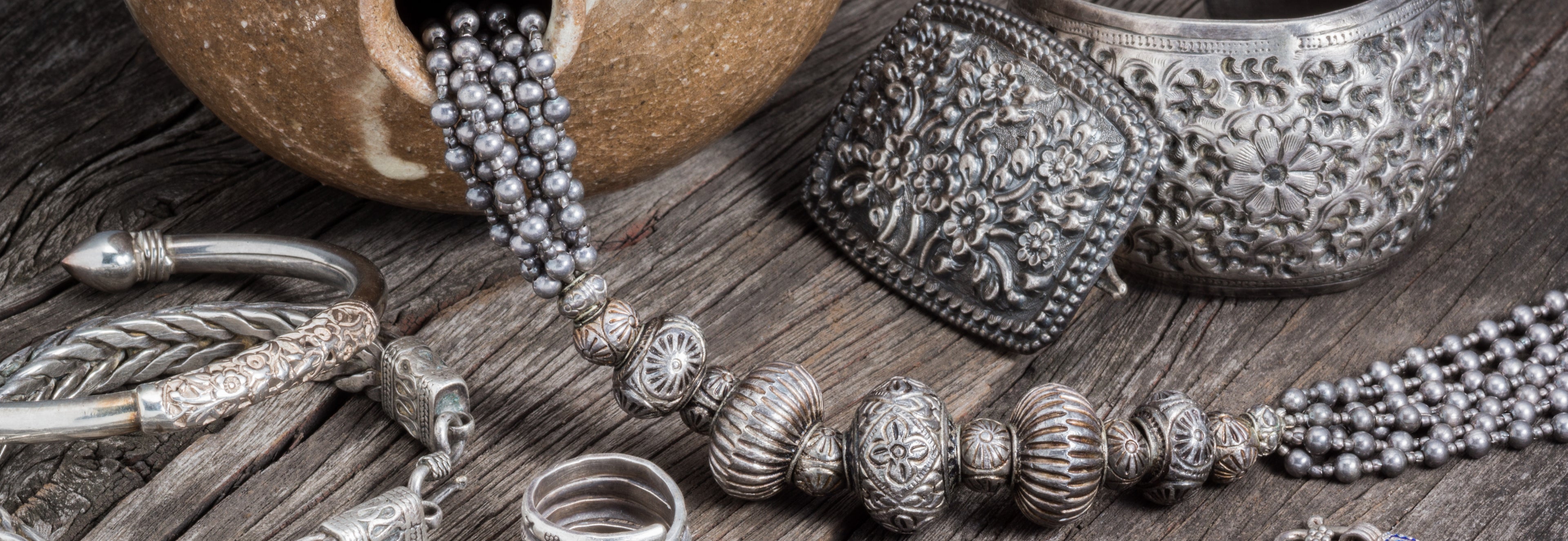 Silver jewelry including bracelets, rings, and necklaces on a wooden surface