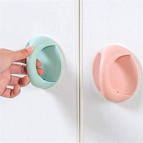 Hand holding a light blue door stopper against a white door with a pink door stopper on the other side.