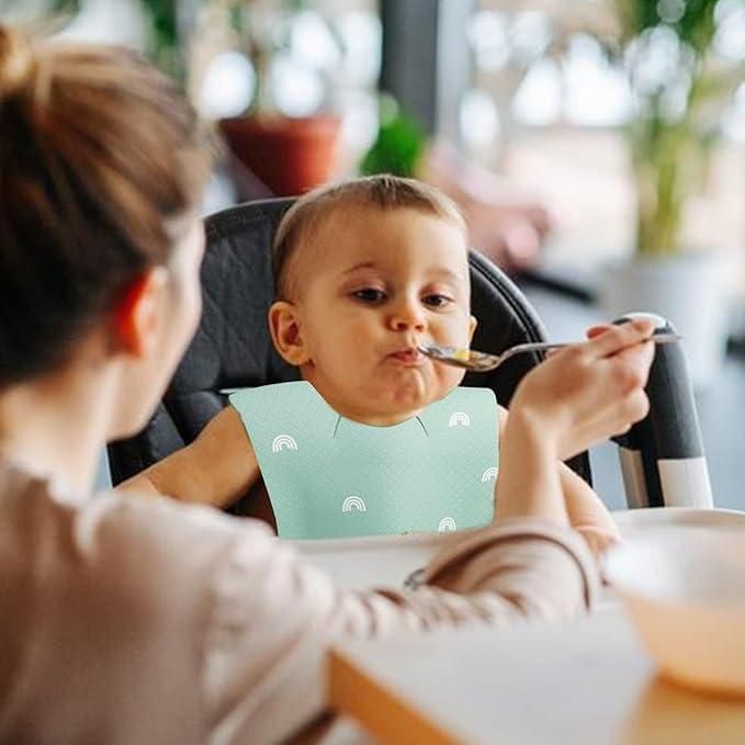Baby being fed by a person with a bib on, sitting in a high chair.