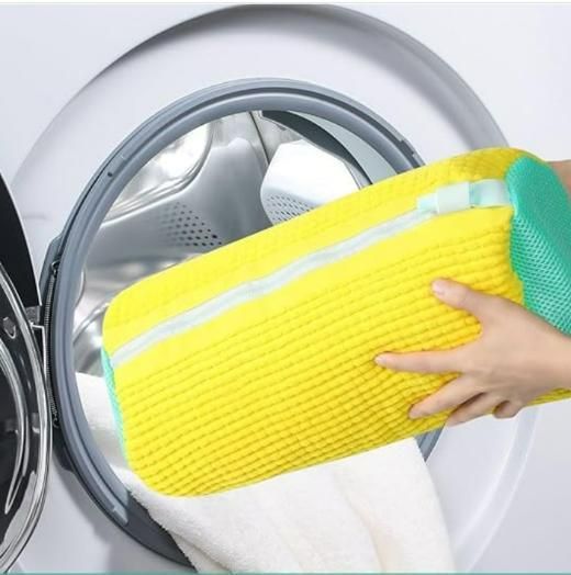 Hand holding a yellow cleaning brush next to a washing machine