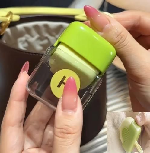 Green and clear container held by a hand with pink nail polish, against a blurred background.