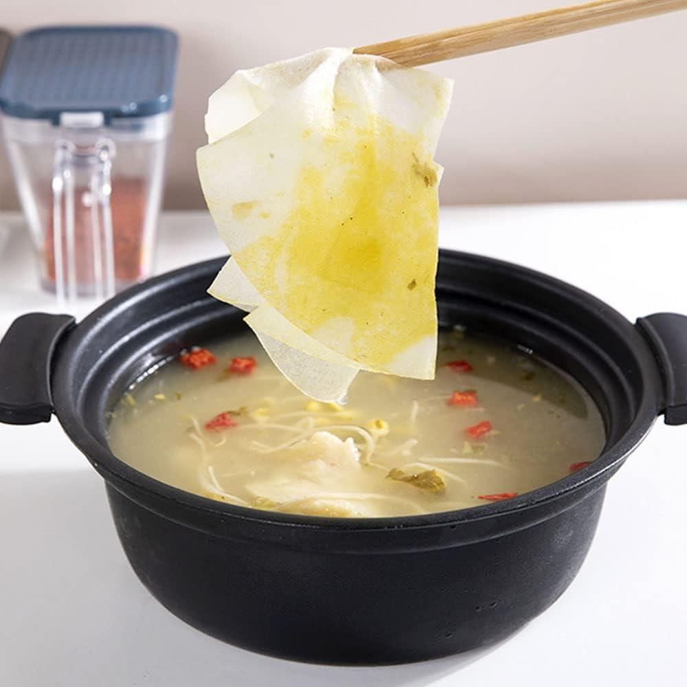 Black pot with soup and a paper bag being dipped into it, with a blurred background.