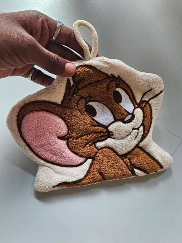 Plush keychain of a cartoon character held by a hand on a light background