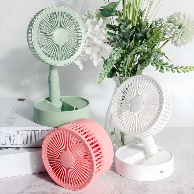 Three small fans in green, pink, and white on a surface with flowers in the background.